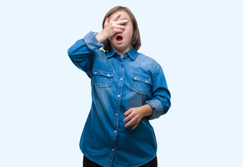 Young adult woman with down syndrome over isolated background peeking in shock covering face and eyes with hand, looking through fingers with embarrassed expression.