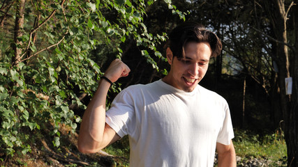 Young handsome man standing in nature, exulting, celebrating, screaming for joy looking at camera