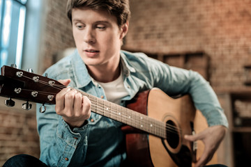 Music instrument. Selective focus of a modern guitar being in hands of a positive nice handsome man