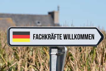 Ein Schild, deutsche Flagge und Slogan Fachkräfte Willkommen