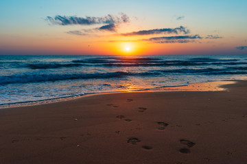 Fototapeta na wymiar Amazing colorful sunrise at sea, footprints in the sand