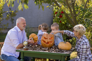 Grandparents enjoying with grandchildren while carving pumpkins together