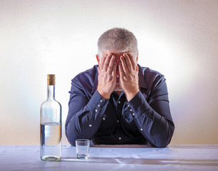 ein Mann sitzt einsam an einem Tisch auf dem eine Flasche und ein Glas mit Alkohol stehen