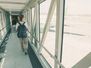 Woman backpacker walking to gate for departure in airport terminal. Window view ariplane waiting, toned, sunny day.