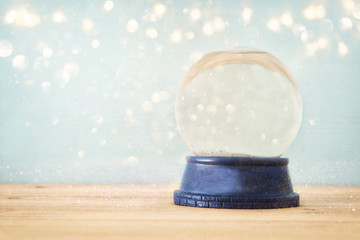 Empty Snow Globe over wooden table with glitter overlay. Magical Christmas concept. Copy space.