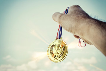 man hand raised, holding gold medal against sky. award and victory concept.