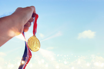 man hand raised, holding gold medal against sky. award and victory concept.