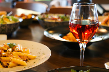Wine, rose, transparent in crystal glass with appetizers. Blur plates with foods background, closeup.