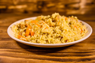 Ceramic plate with pilaf on wooden table