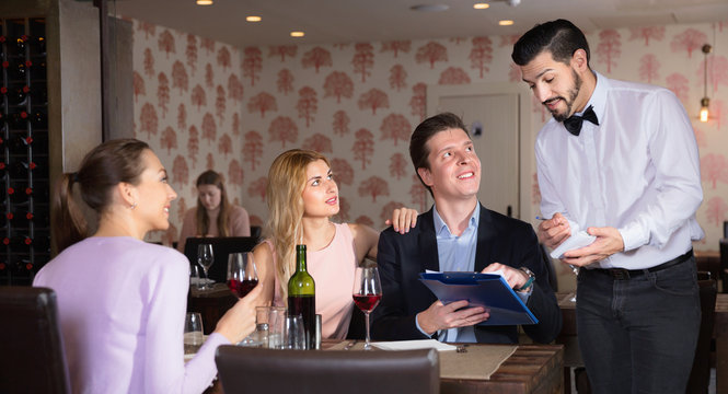 Handsome waiter taking order from young people in restaurant