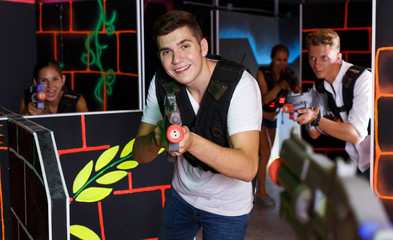Smiling people in vests and with laser pistols playing emotionally laser tag game