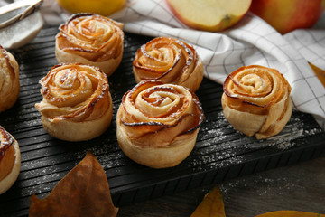 Wooden board with apple roses from puff pastry on table, closeup