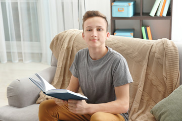 Teenage boy reading book at home