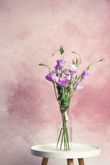 Vase with bouquet of beautiful flowers on table against color background