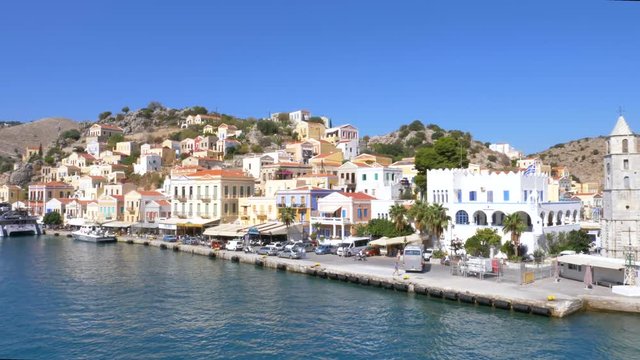 Low angle aerial footage of the beautiful island of Symi (Simi) with Colorful houses and small boats at the heart of the village bay.