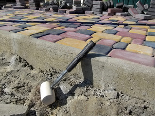 Work on laying paving slabs, bright colorful background. A white rubber hammer leans a high curb,...