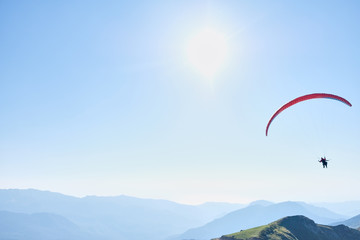 Parachute with one person glides across the clear sky over a beautiful mountain landscape. Non-urban scene. Travel destination. Sports activities