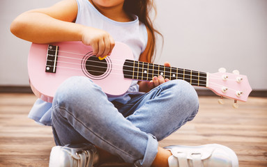 Cute little girl playing pink ukulele sitting on floor