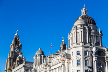 Fototapeta na wymiar The three buildings (Port of Liverpool Building, Cunard Building and Royal Liver Building) which make up the Three Graces on the Liverpool waterfront under a blue sky.
