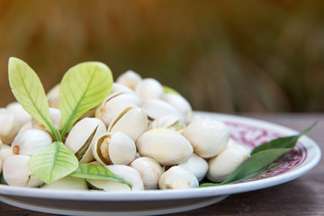 Close up of Pistachios nuts on wooden table. Pistachio in wooden bowl in background with green leaves