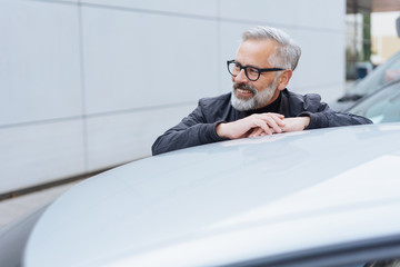 lächelnder älterer mann lehn auf seinem Autodach