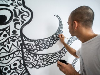 Closeup artist painting abstract pattern in octopus shape on white cement wall.