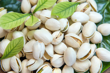 Close up of Pistachios nuts on wooden table. Pistachio in wooden bowl in background with green leaves