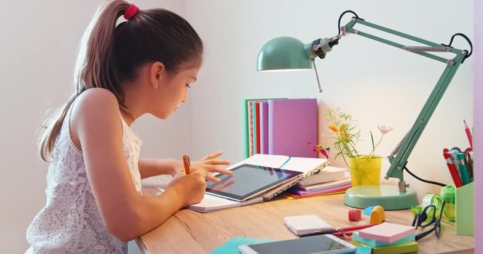 Pretty teenage girl writing a letter in notebook at school and looking at the camera