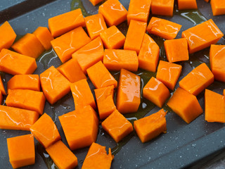 Chopped pumpkin being drizzled with olive oil before baking on a tin