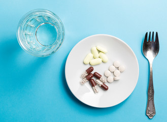 A fork with a pile of medicines and a glass of water.