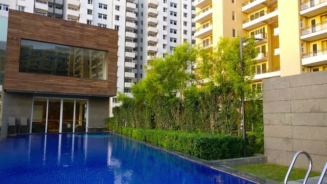 Pan up shot of swimming pool going to modern sky scraper building in gurgaon. This shot showcases the luxury ameneties in modern apartment complexes and how well the living standards are