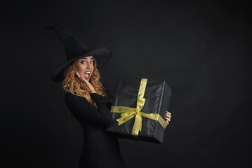 Black Friday. Halloween witch with a black hat on a black background holding gift boxes with juruse in her hands. Surprise and gift on sale
