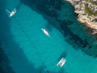 Aerial bird's eye view drone of boat docked in mediterranean tropical beach with turquoise - sapphire waters