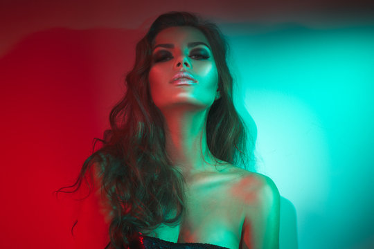 Fashion model brunette woman in colorful bright neon lights posing in studio. Beautiful sexy girl, trendy glowing makeup, metallic silver lips