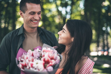 Thankful woman. Cheerful thankful young woman kindly smiling to her positive beloved man after receiving a bouquet of flowers from him