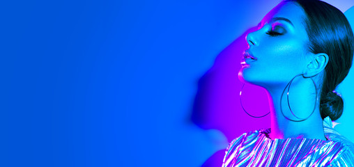 Fototapeta premium Mody modela brunetki kobieta w kolorowych jaskrawych neonowych światłach pozuje w studiu. Piękna seksowna dziewczyna, modny świecący makijaż, metalowe srebrne usta
