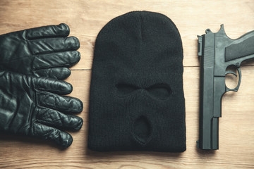 Pistol, balaclava and gloves on wooden background. Criminal concept