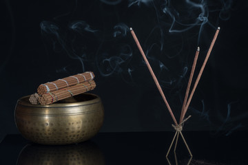 Burning incense sticks and singing bowl isolated on black background