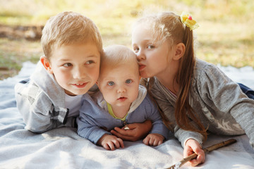 Three children, elder brother, sister blonde and 7-month-old boy with blue eyes are lying on a rug in the autumn forest.