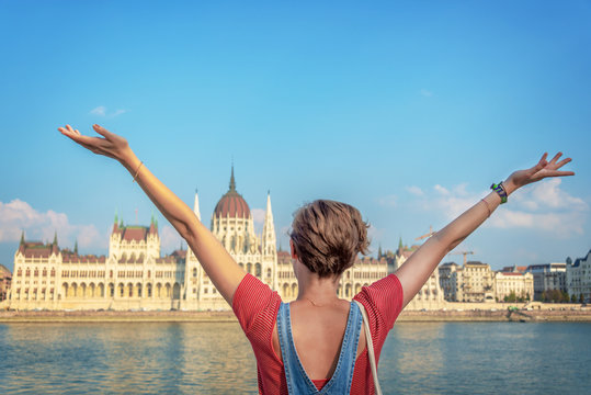 Happy girl, young woman raising her arms in front of Danube river and Budapest parliament, travel or study in Hungary