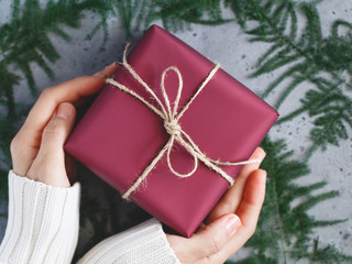 Girl's hands in a winter white warm sweater are held a Red Christmas gift box is tied of twine...