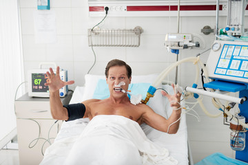 Portrait of enraged patient on mechanical ventilator lying in bed and looking at camera with...