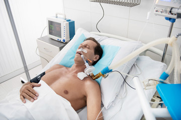 Get well soon. Portrait of middle aged gentleman with endotracheal tube in the mouth sleeping in recovery room after surgery