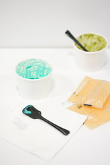 Empty ice cream cup. 2 empty paper takeaway cups with remains of mint and green tea ice cream & plastic black spoons.  Soft focus on the black spoon with mint ice cream. Leftover dessert on the table.