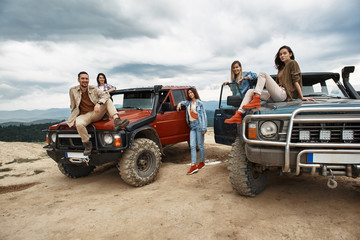 Joyful young people travelling in the mountains while resting on off road cars