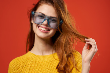 happy woman in blue glasses and yellow sweater touches hair with her hand