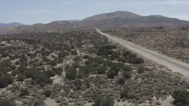 Aerial pullback of a road in a barren desert land with some small shrubs.