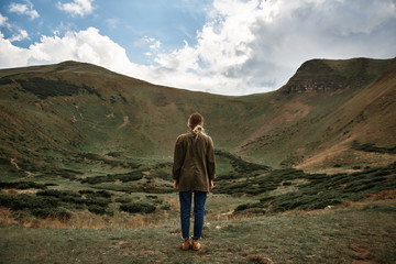 Fototapeta premium Woman and nature. Calm experienced traveler standing in front of the mountains and enjoying the view while being alone