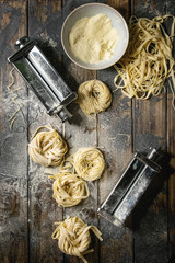Variety of italian homemade raw uncooked pasta spaghetti and tagliatelle with pasta maker rolled machine and semolina flour over dark plank texture wooden table. Flat lay, space