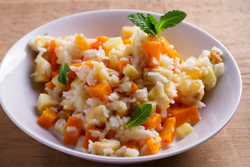 Rice porridge with pumpkin, apples and raisins in white bowl. Vegetarian diet dish of rice and pumpkin. Healthy food. horizontal